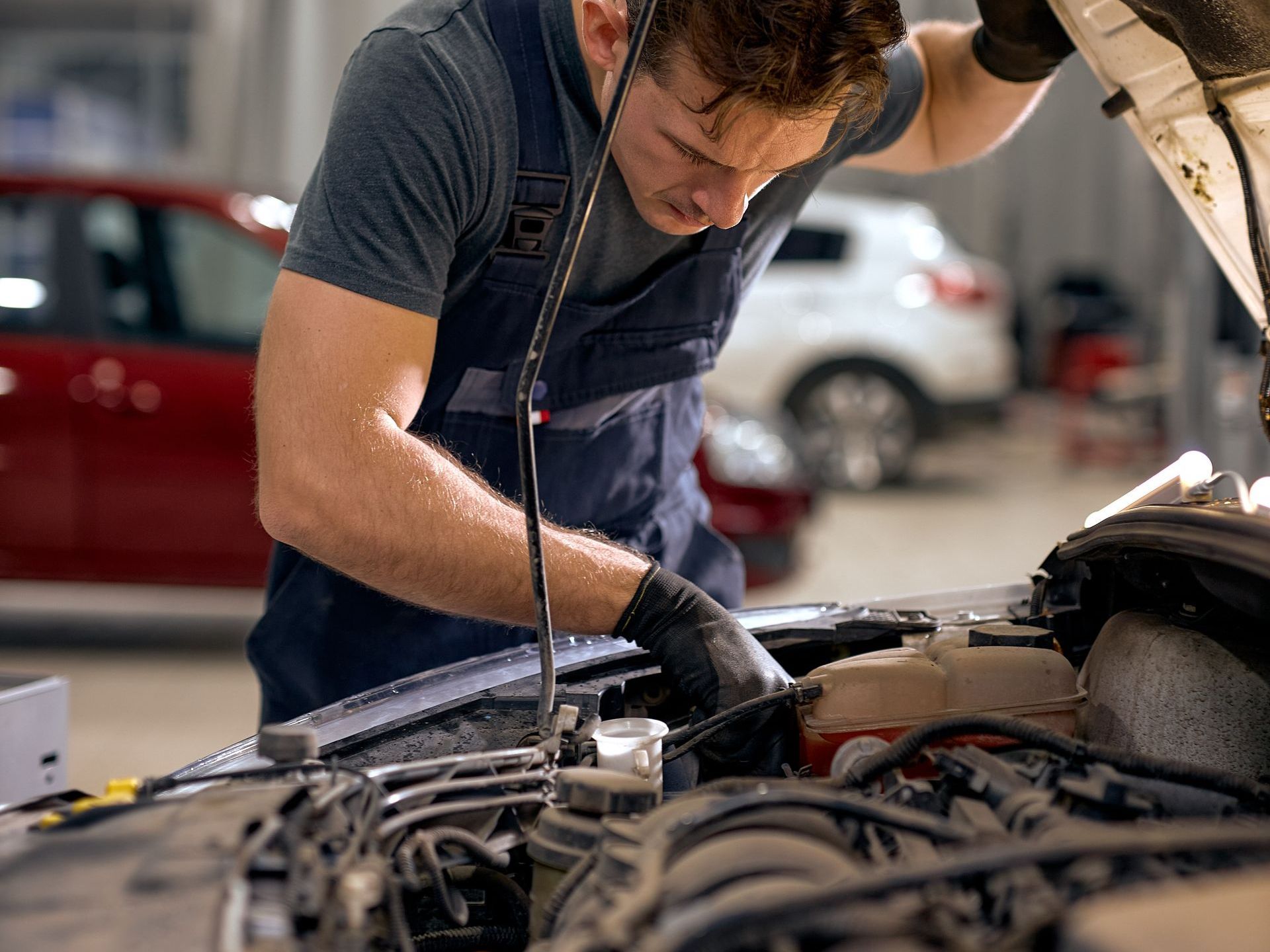 Mechanic in blue overalls working on a car engine in a garage. | Railside Auto Service