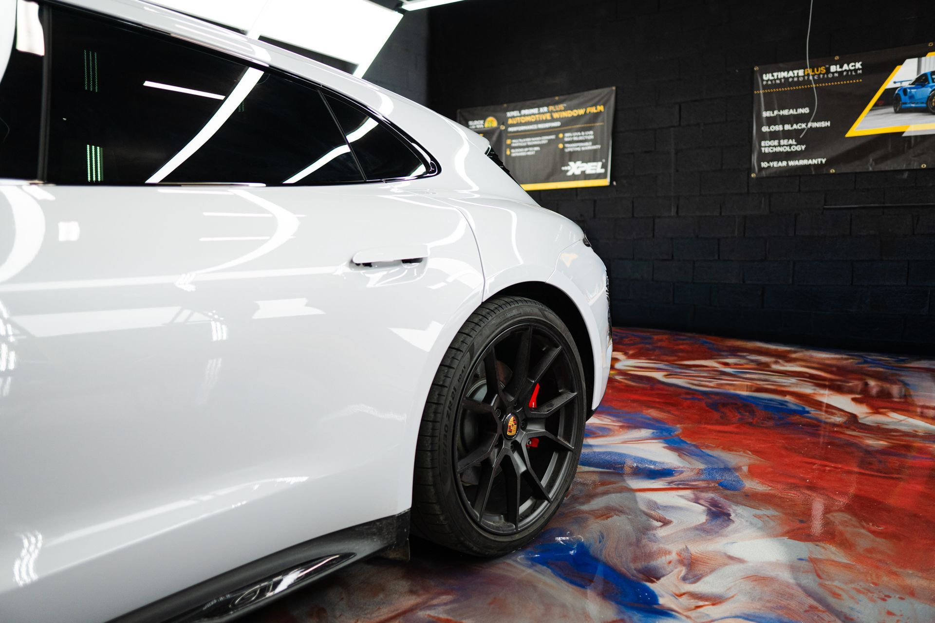 White car's side, black wheels, red brake calipers, glossy finish. Interior shot with reflective flooring.