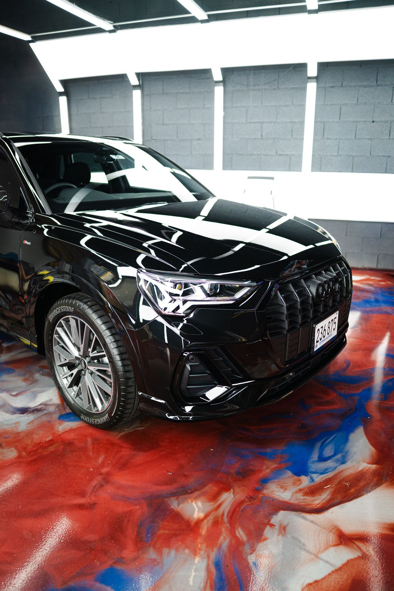 Black Audi SUV parked on a colorful epoxy floor in a garage setting.