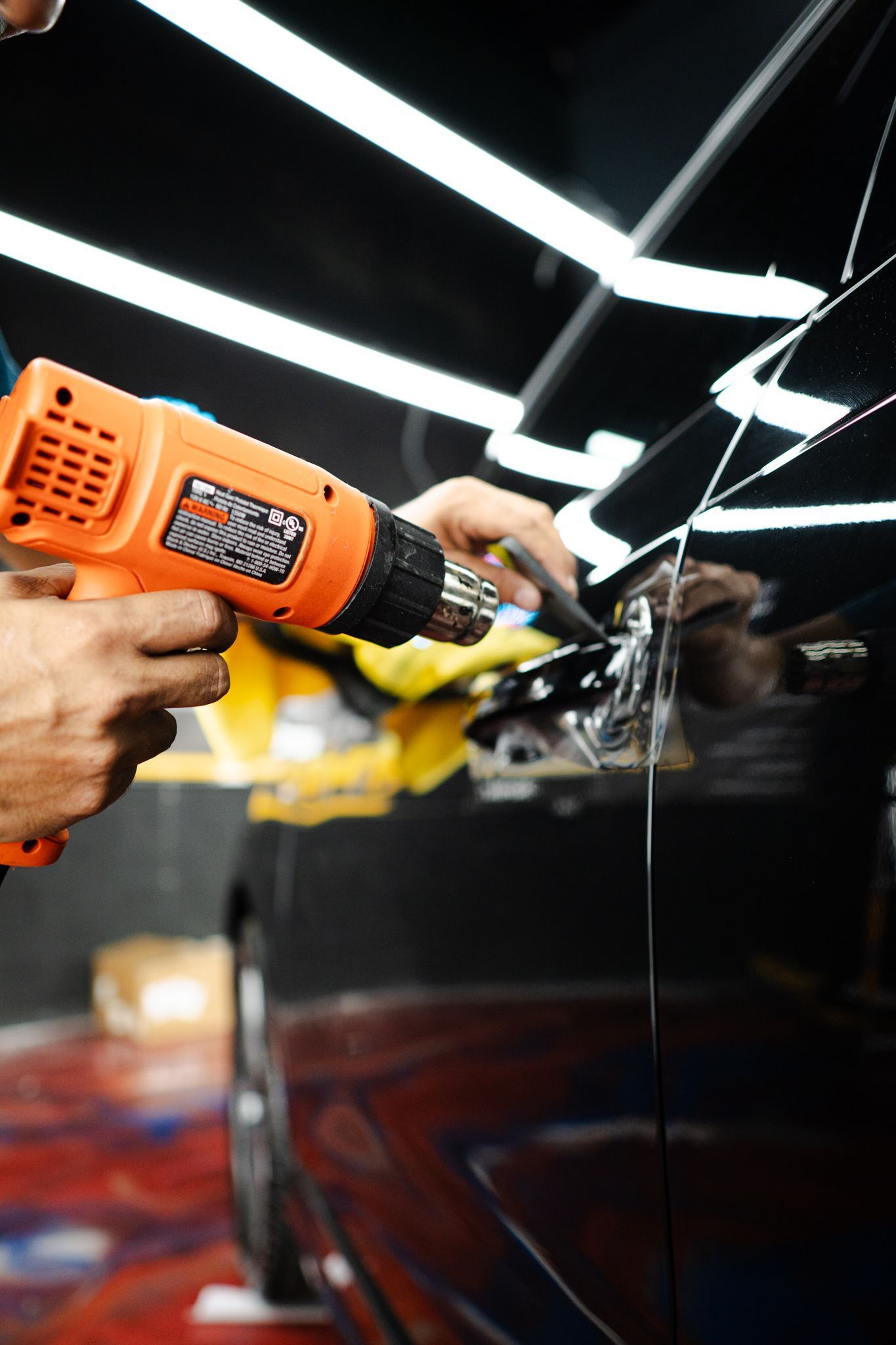 Person using a heat gun on a black car door to apply protective film.