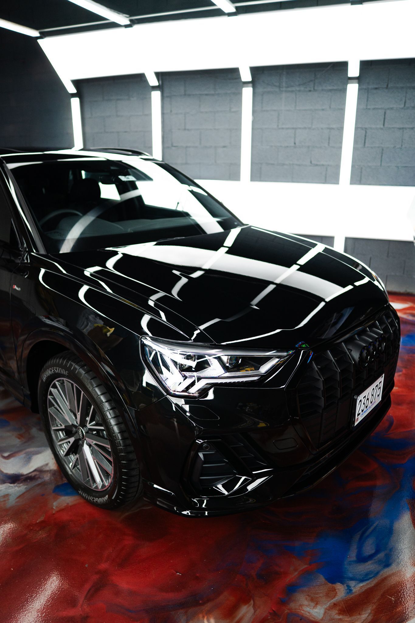 Black Audi SUV, glossy finish, parked inside with bright overhead lights. Reflective paint.