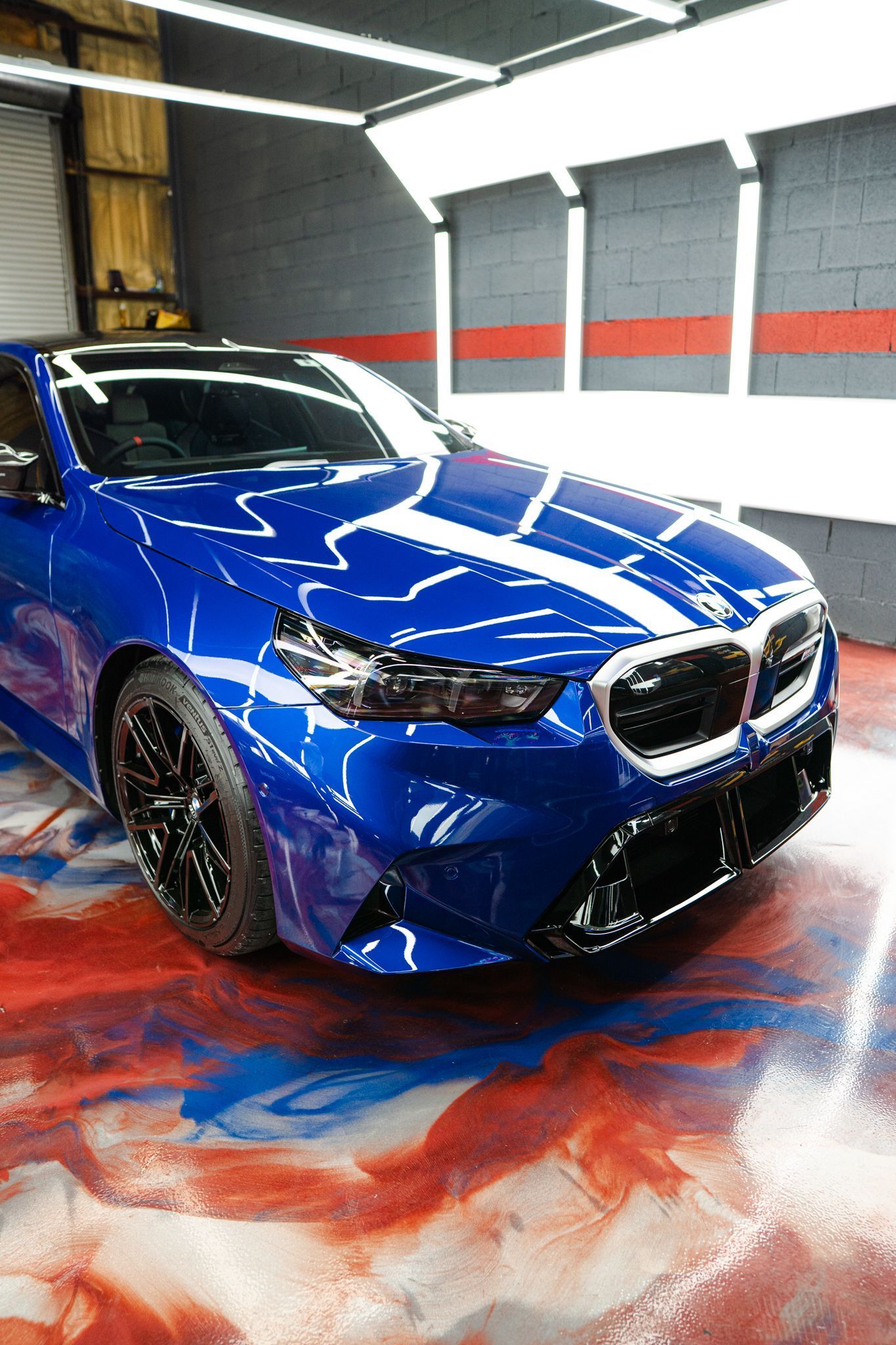 Blue BMW in a well-lit garage, reflecting on a colorful epoxy floor.