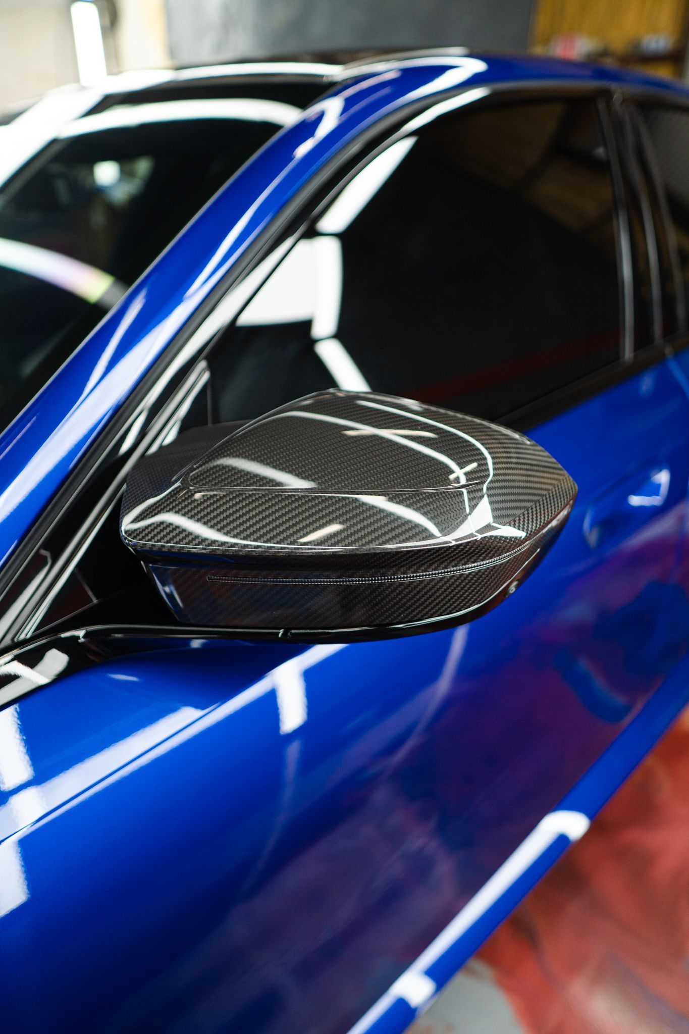 Blue car with a carbon fiber side mirror reflecting the surroundings.