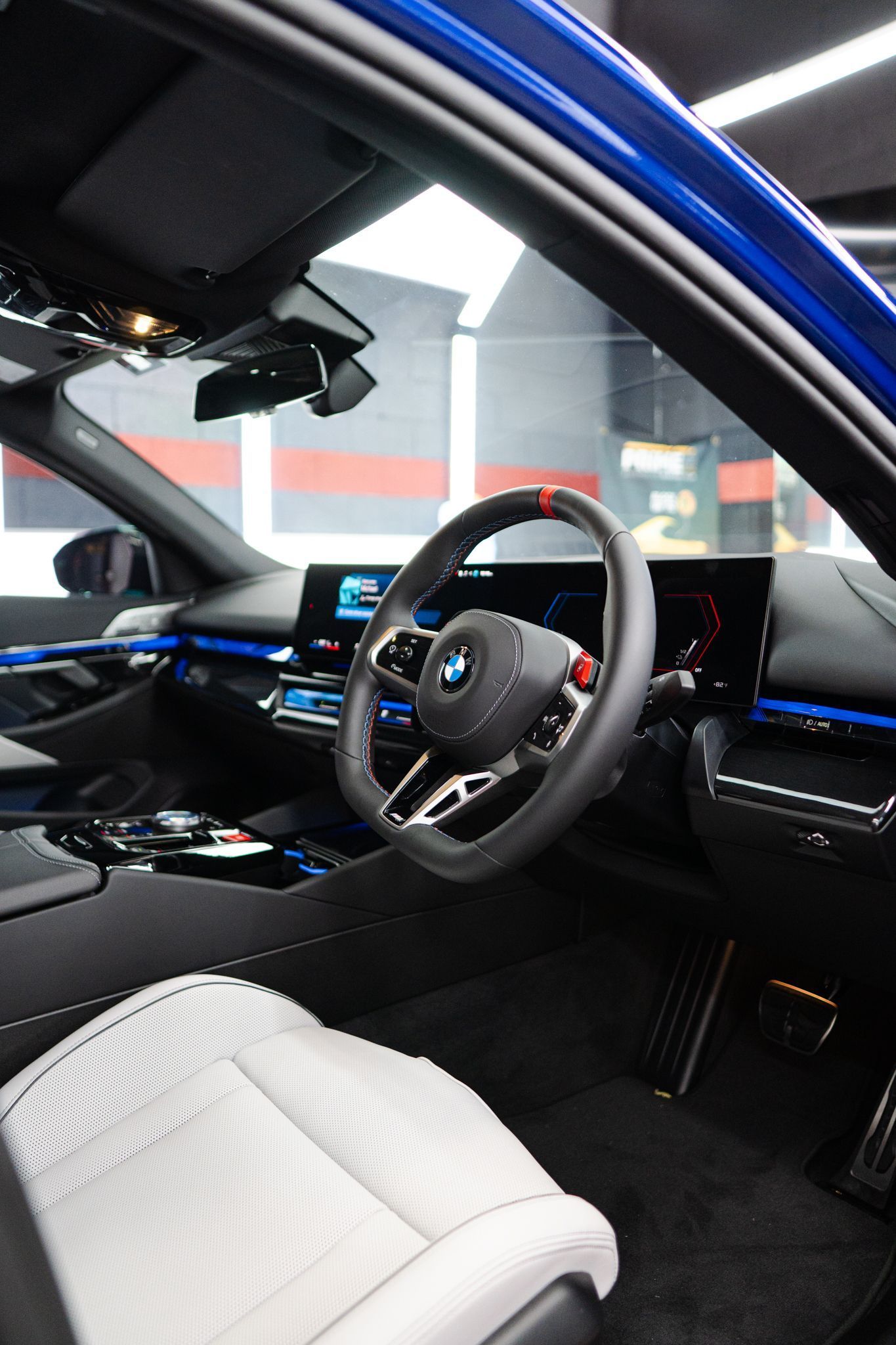 Interior view of a blue BMW car. Black dashboard, steering wheel, and white seat.