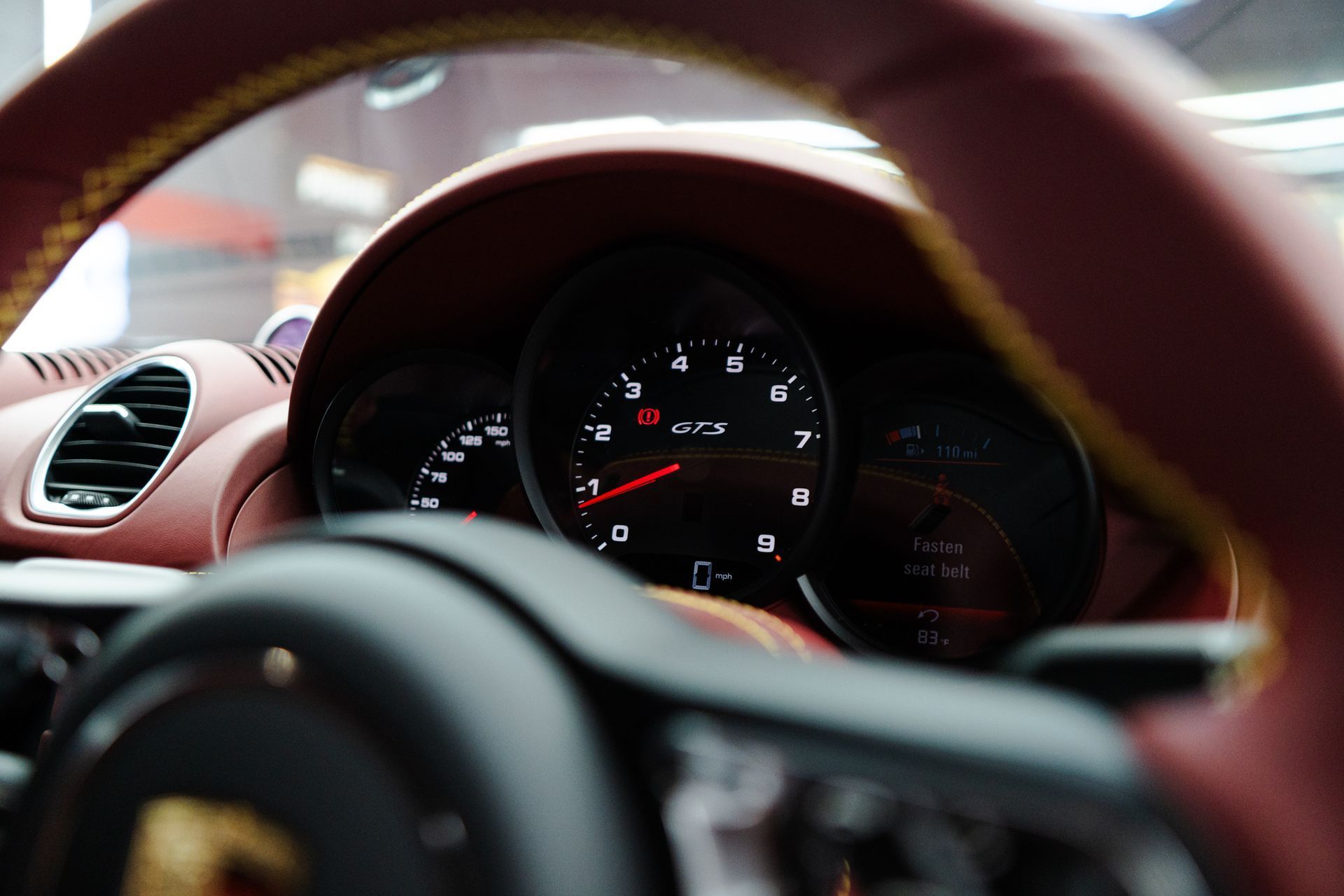Dashboard of a red and black Porsche car with a steering wheel and gauges in view.