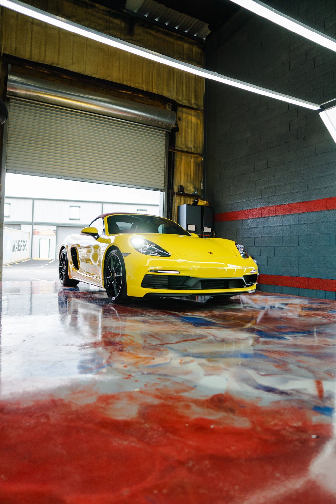 Yellow Porsche exiting a garage with a wet, reflective floor.