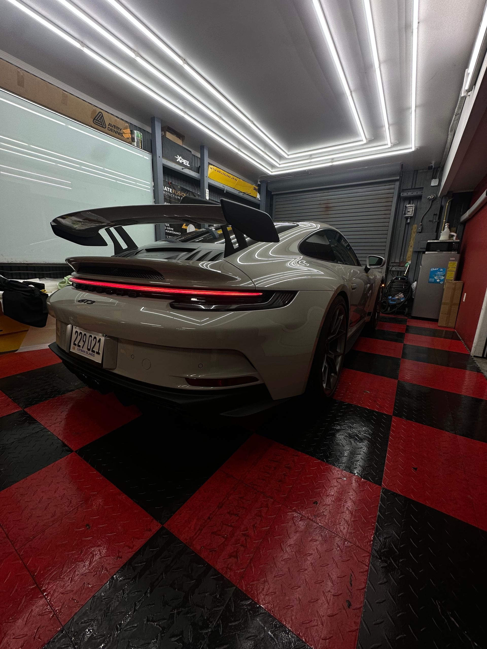Gray sports car with large rear wing in a garage with red and black checkered floor.