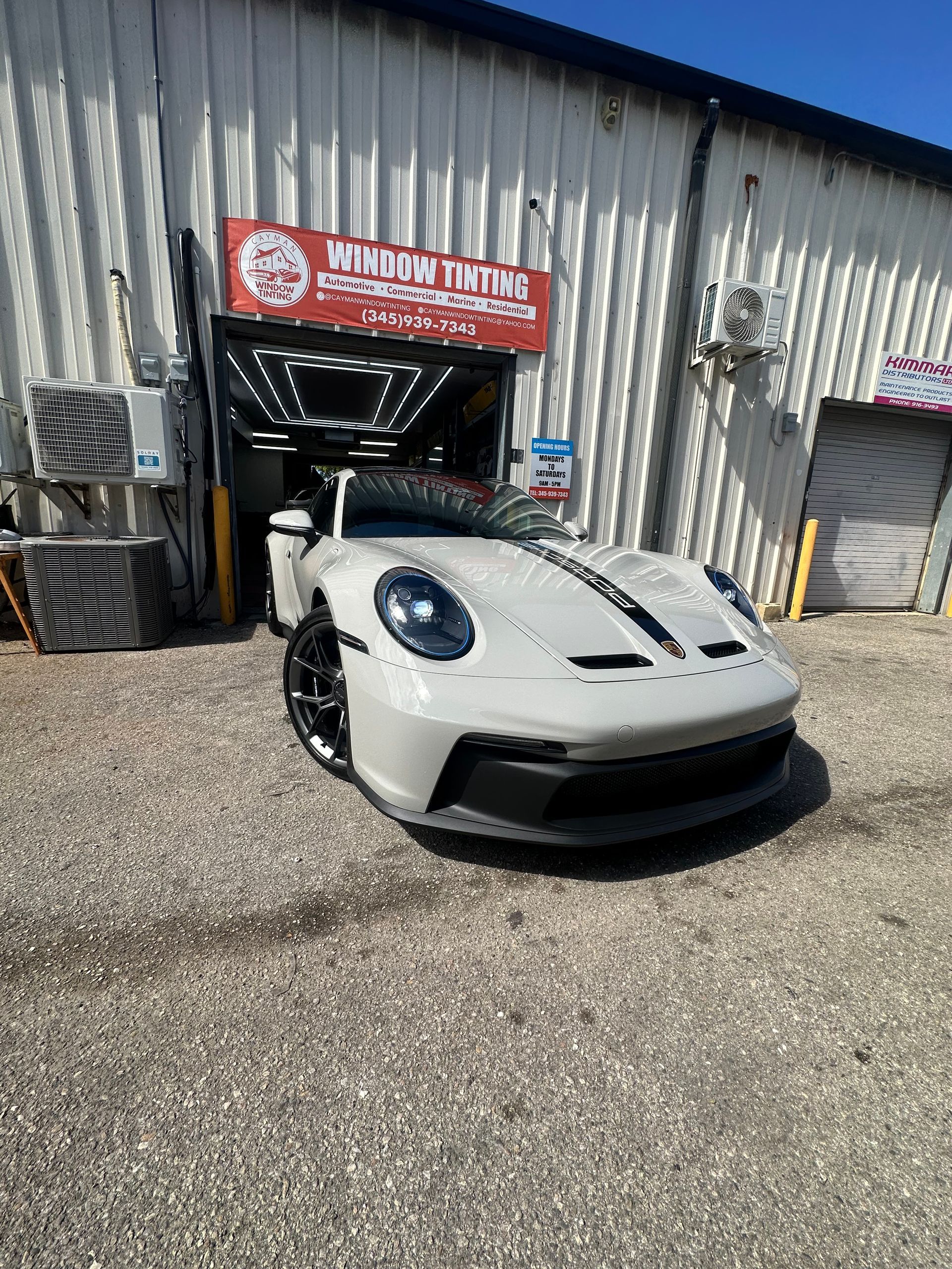 White Porsche 911 GT3 with black stripes parked in front of a window tinting shop.