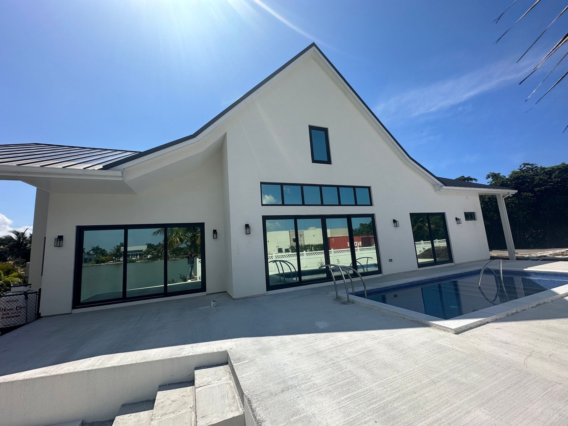 White modern house with a pool and dark-framed windows against a blue sky.