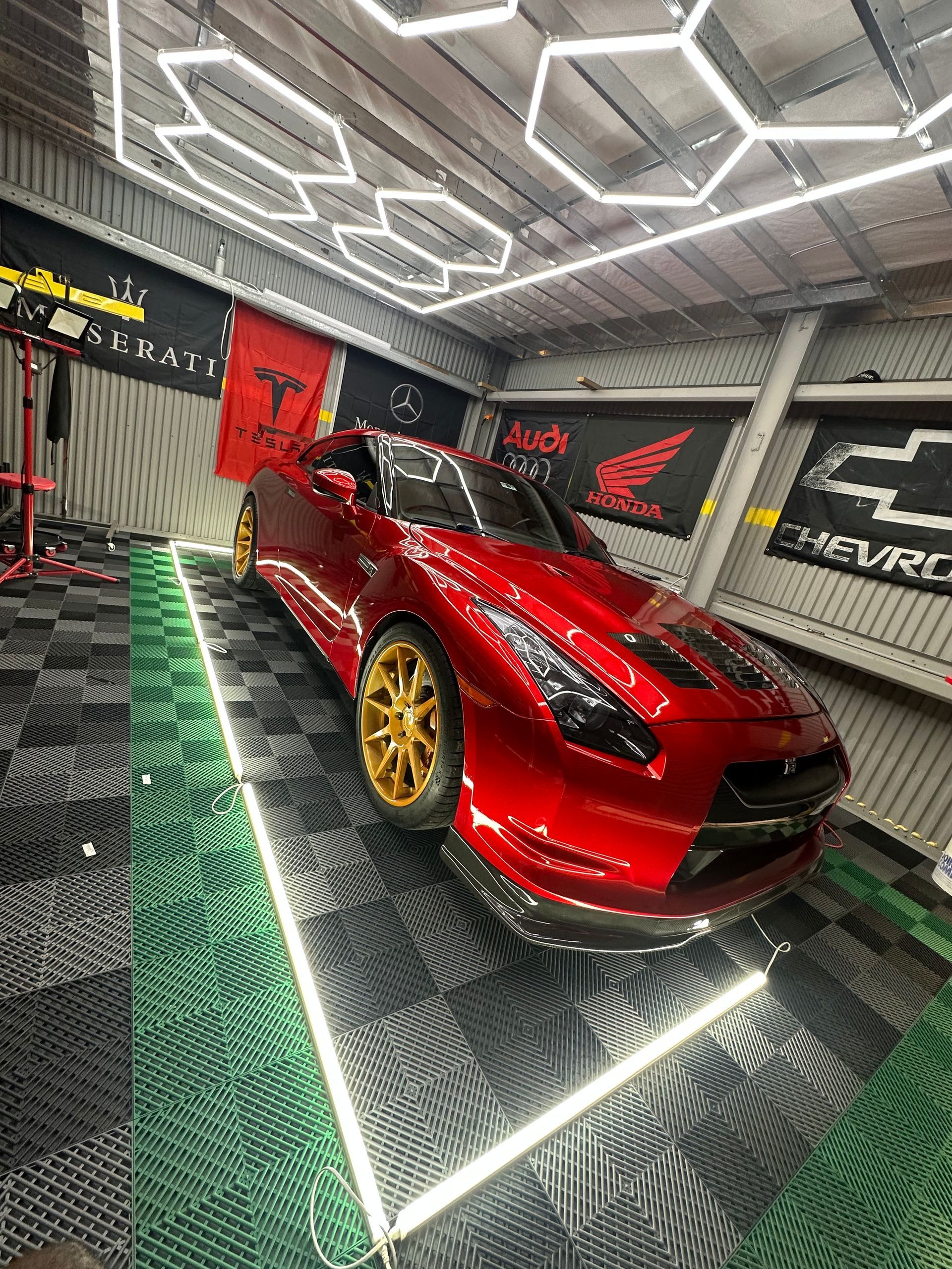 Red Nissan GT-R sports car on a checkered garage floor with gold rims, under hexagon lights.