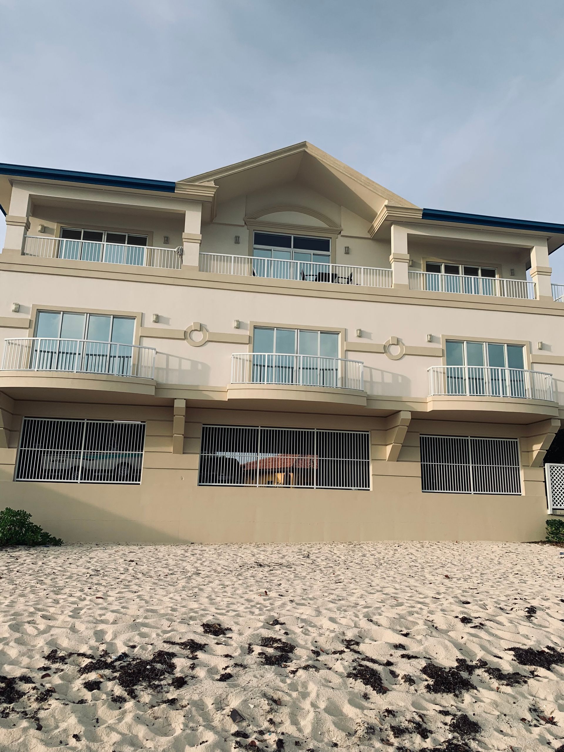 Beige building with balconies, reflecting distorted light, on a sandy beach.