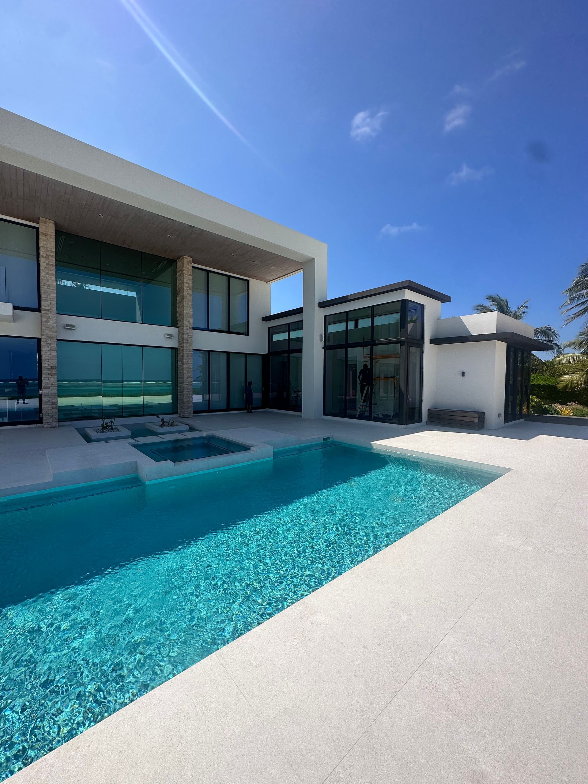 Modern house with turquoise pool, clear sky, and light-colored patio.