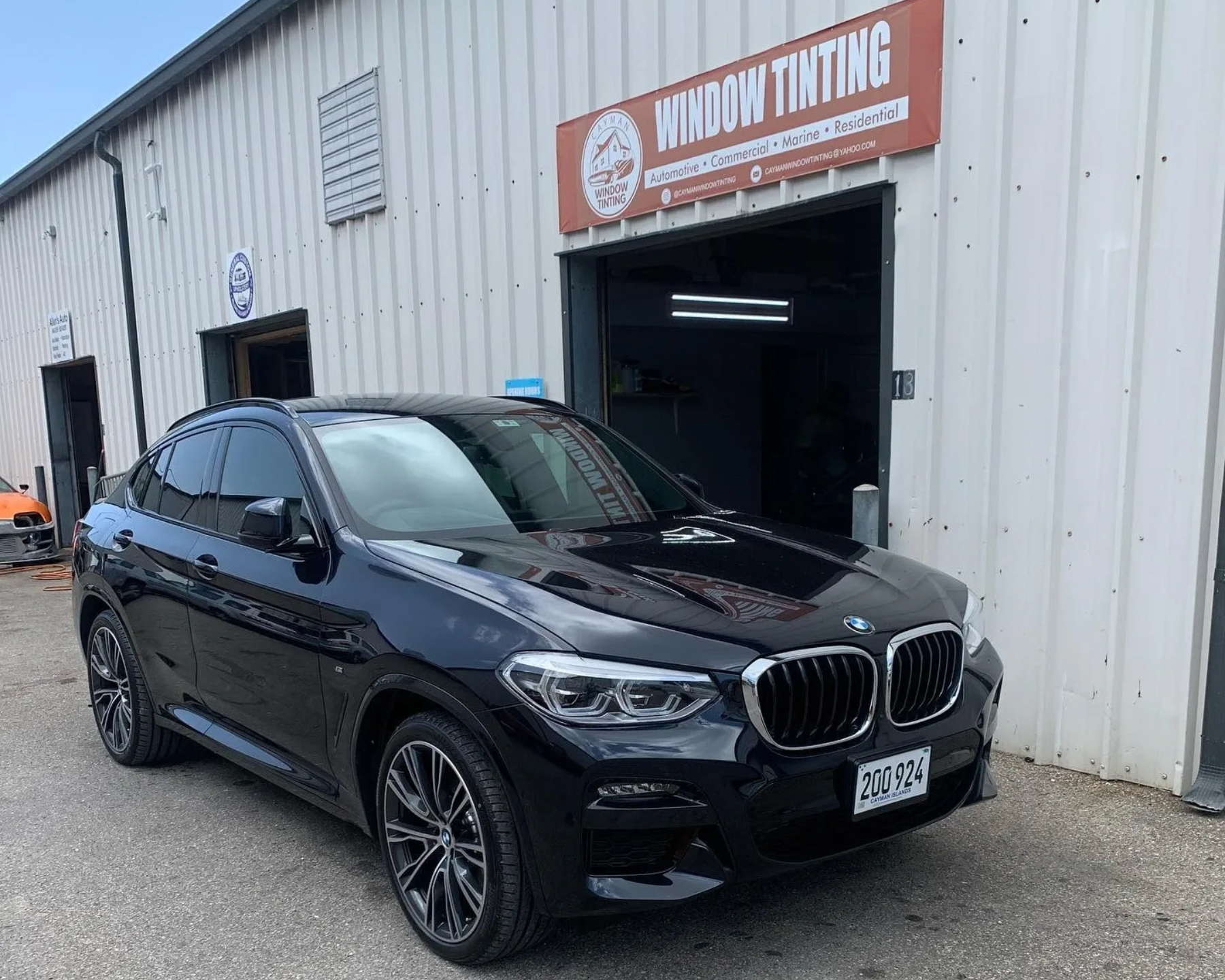 Black BMW X4 with tinted windows parked in front of a window tinting business.