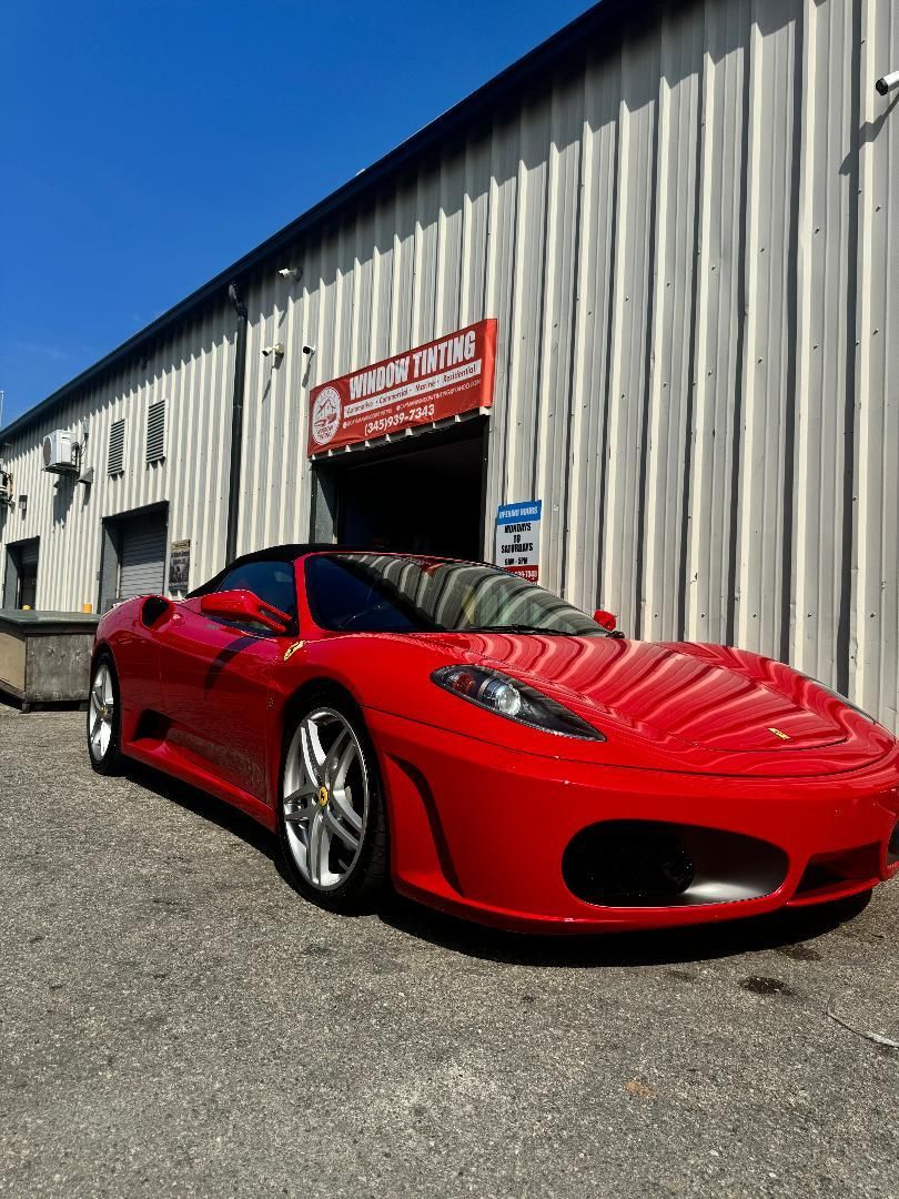 Red Ferrari sports car parked in front of a repair shop on a sunny day.