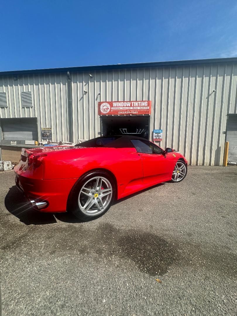 Red Ferrari convertible parked in front of a commercial building with a blue sky.