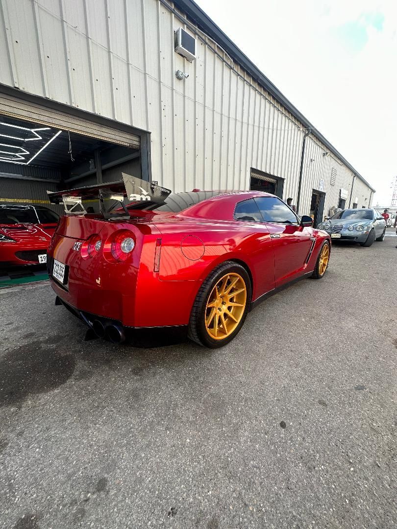 Red Nissan GT-R with gold wheels parked outside a building; other cars are visible nearby.