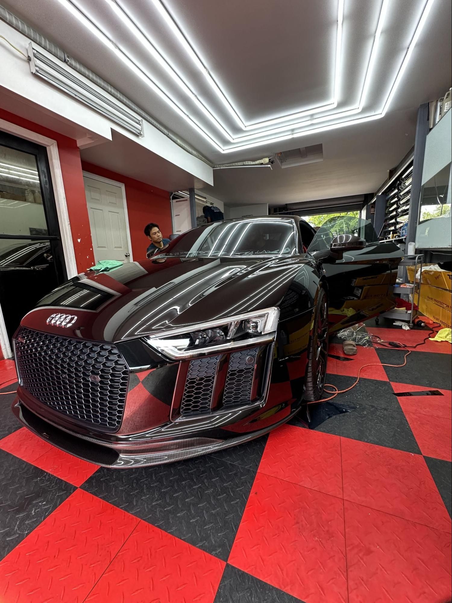 Inside a clean auto detailing shop, a professional detailer applies ceramic coating to a black car.