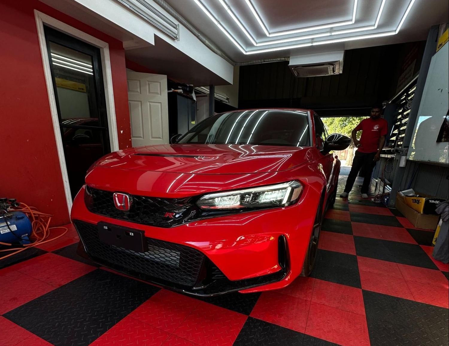 A red car is parked in a garage with a checkered floor.