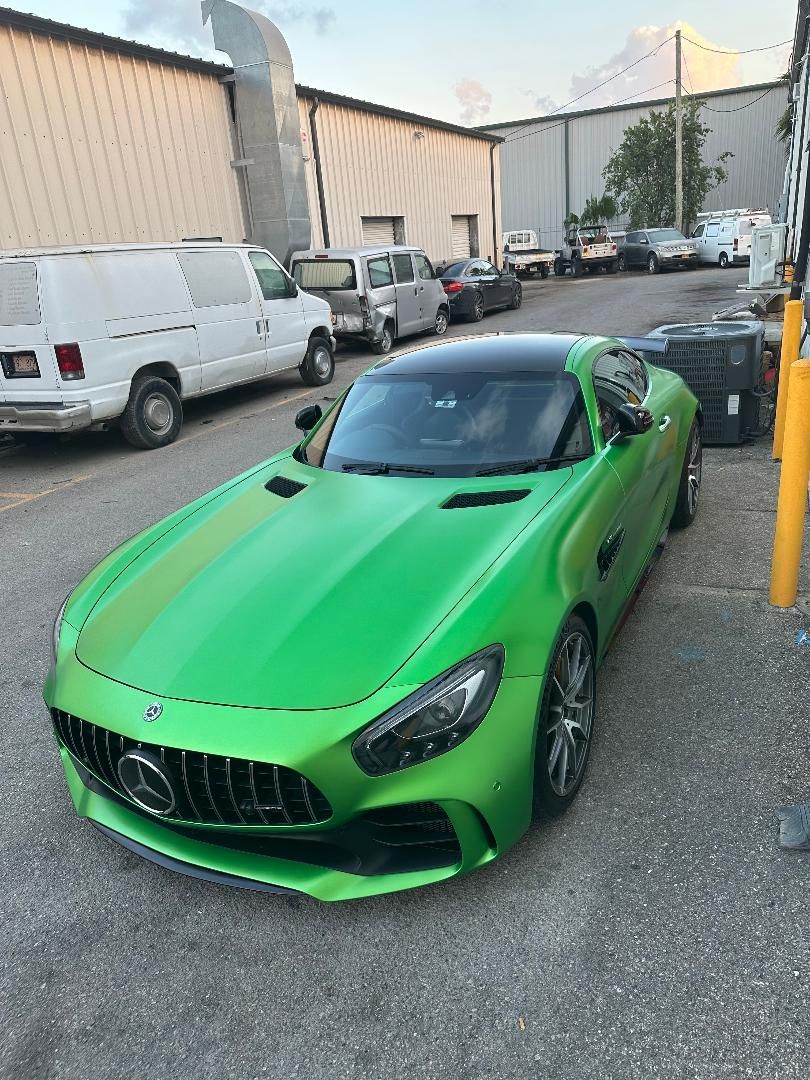 Green Mercedes-AMG GT coupe parked in an industrial setting. Black roof.