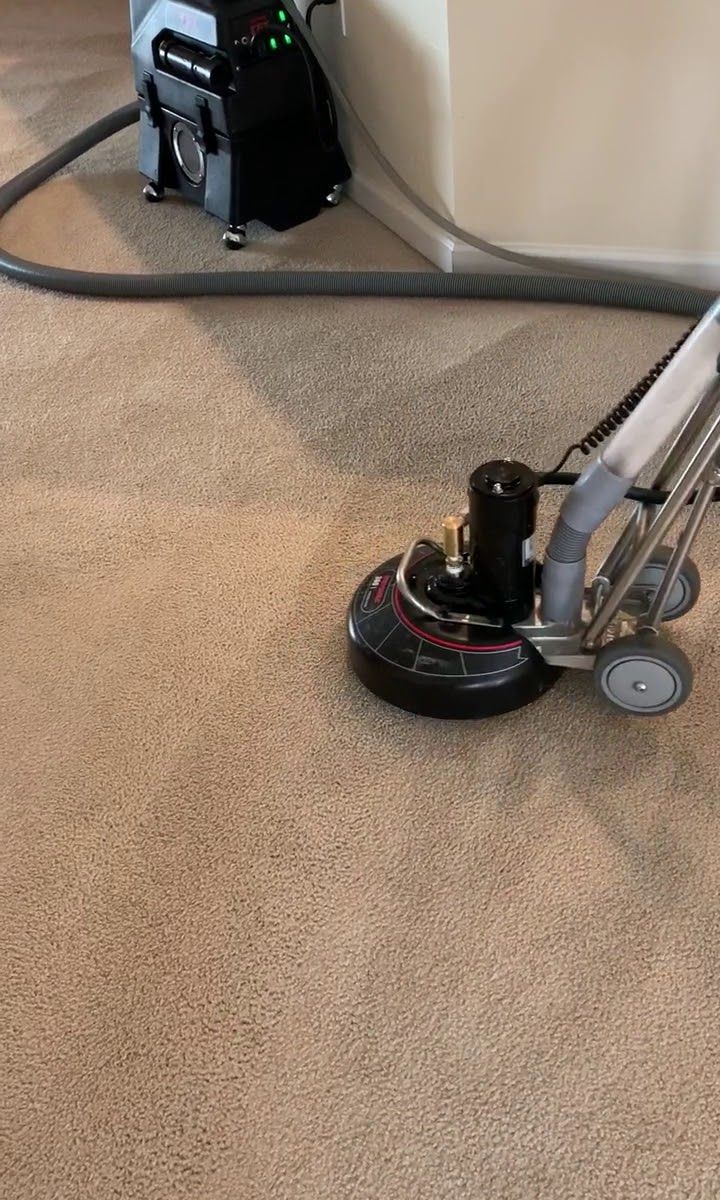 Carpet cleaning machine scrubbing a tan carpet in a room.