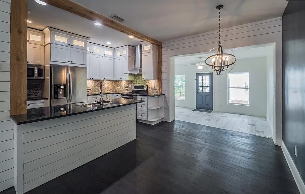 Kitchen with white cabinets, black countertop, and dark wood floors; entryway in the background.