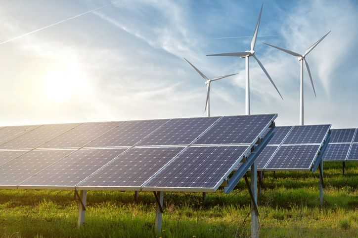 Uma fileira de painéis solares e turbinas eólicas em um campo.