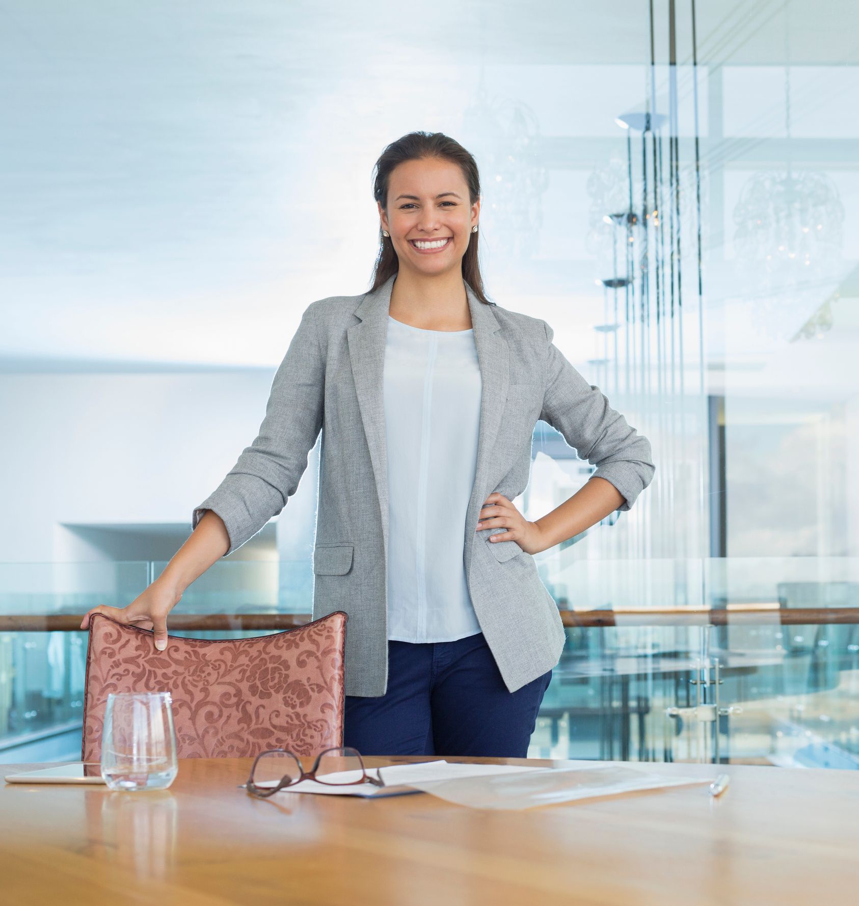 Uma mulher empreendedora de uma Microempresa diante de uma mesa e as mãos na cintura