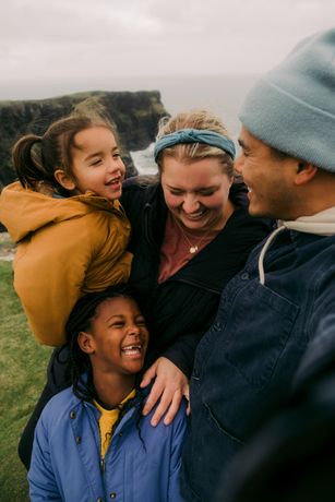 A family is posing for a picture on top of a cliff near the ocean.