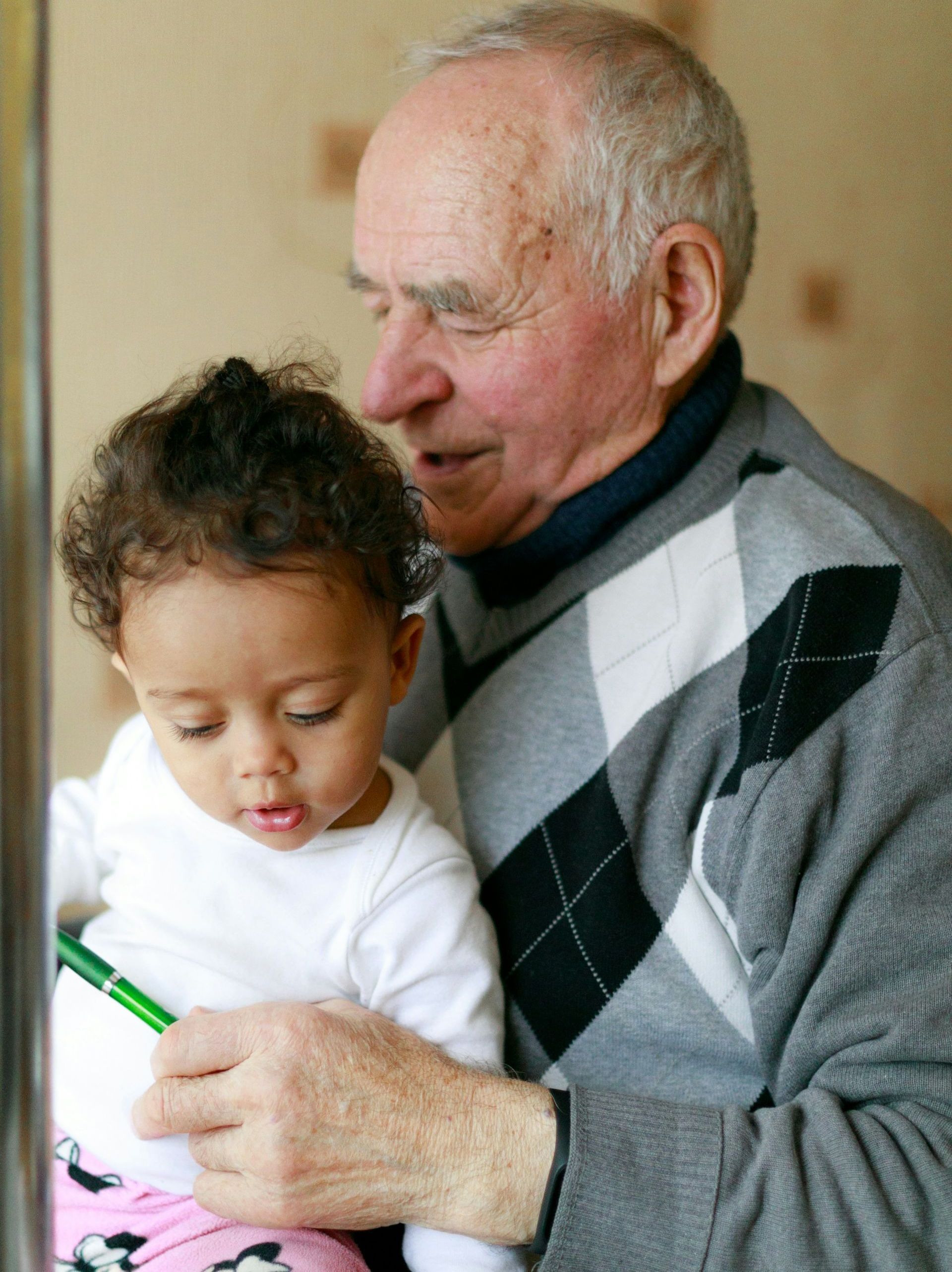 An elderly man is holding a little girl who is holding a pencil