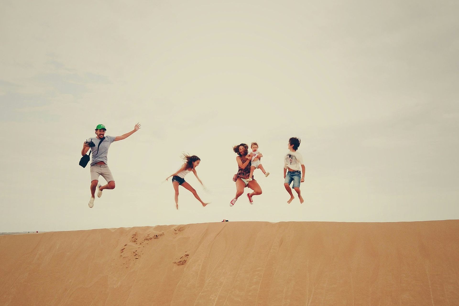 A group of people are jumping in the air on top of a sand dune.