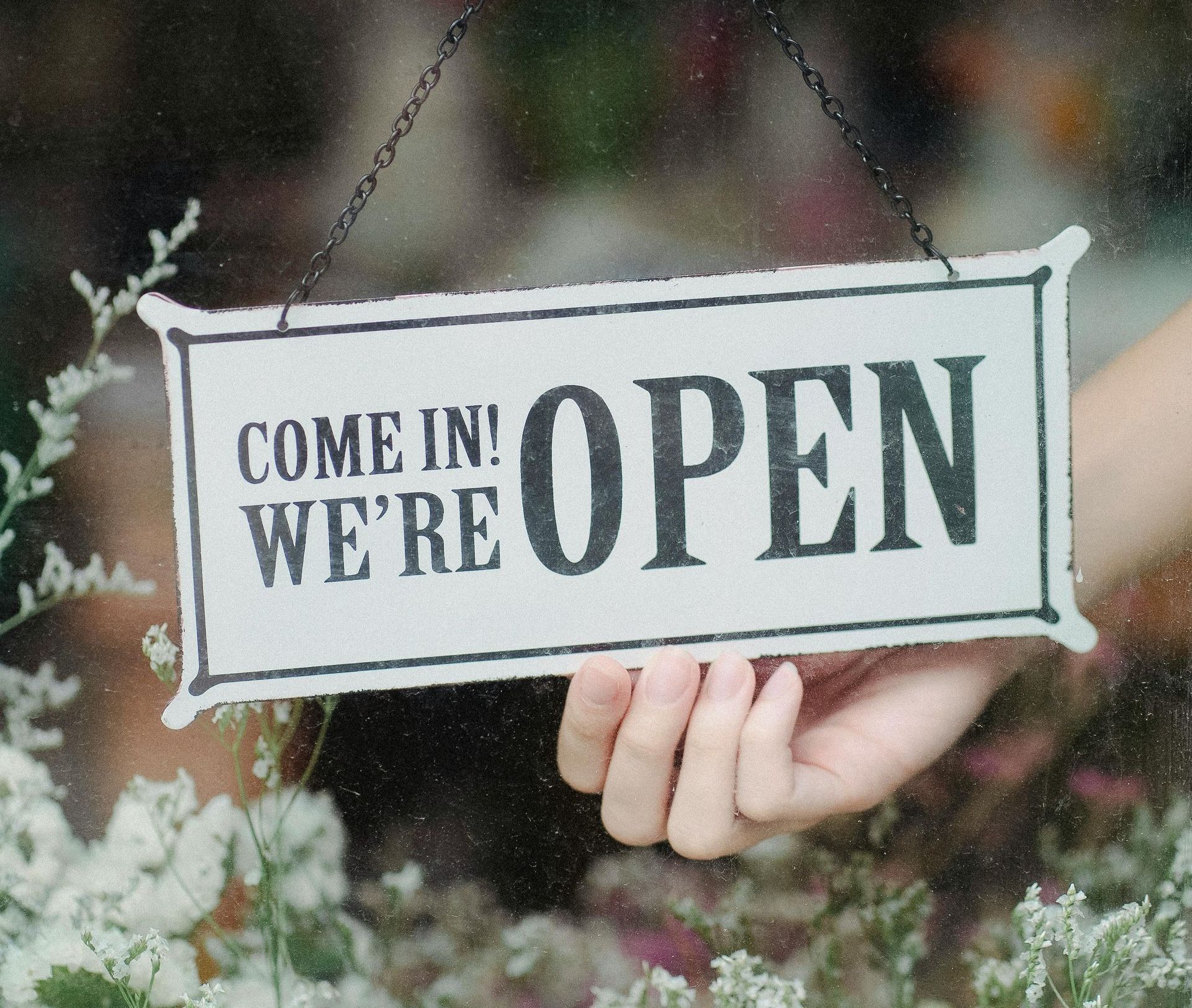 A person is holding a sign that says come in we 're open