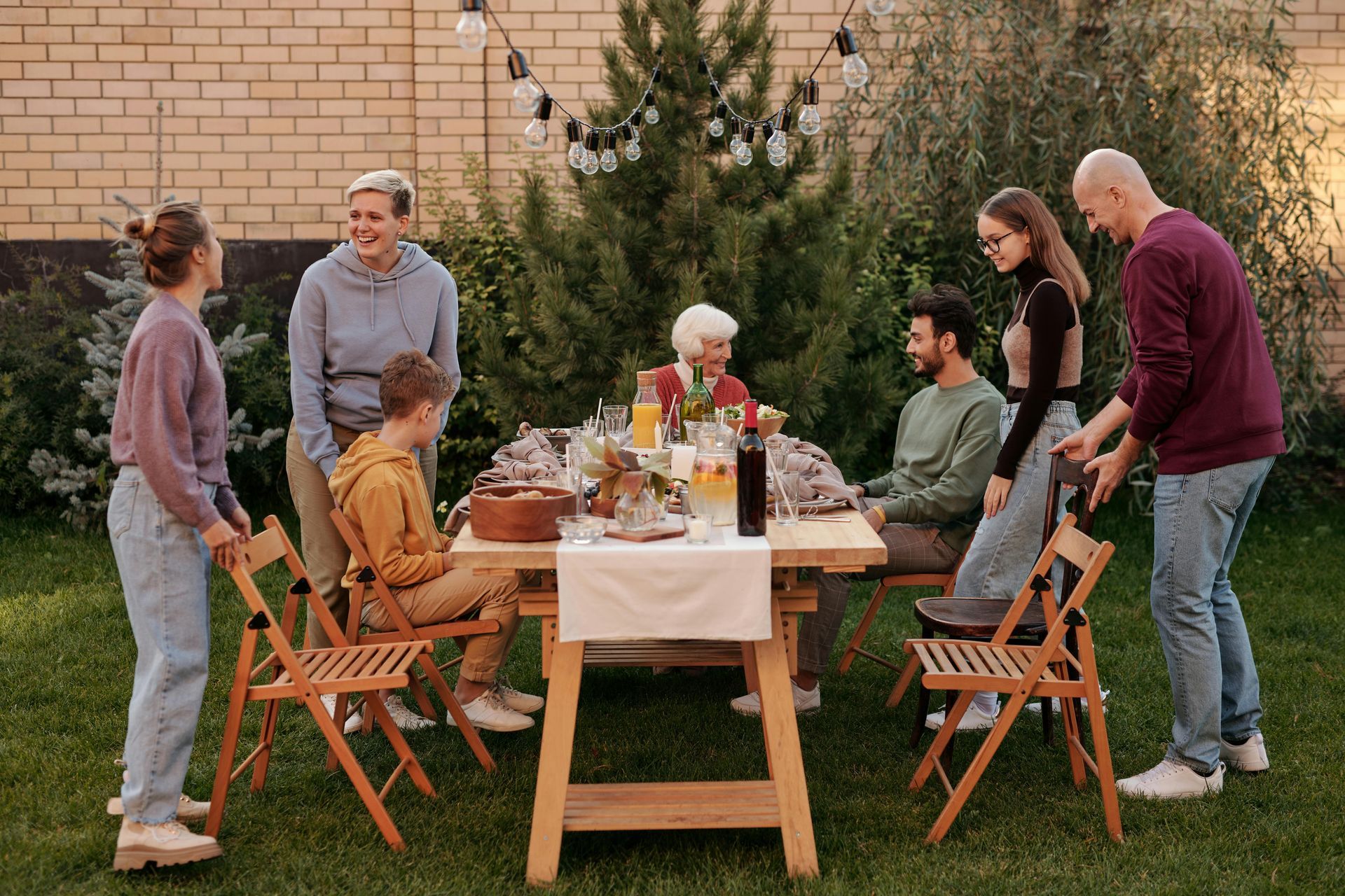 A group of people are sitting around a table in a backyard.