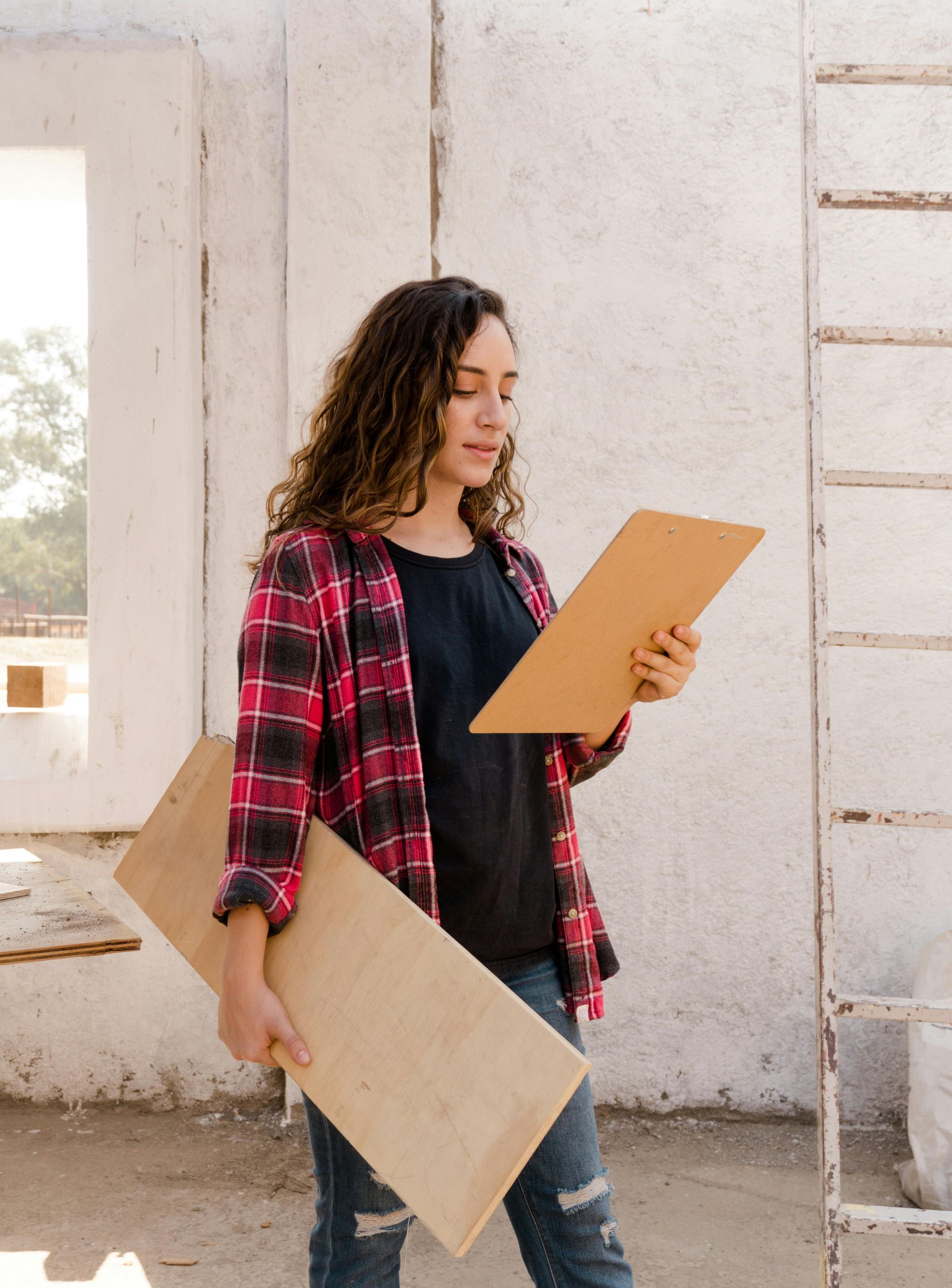 A woman in a plaid shirt is holding two pieces of wood.