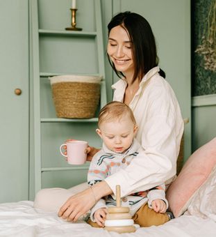 A woman is sitting on a bed with a baby and a cup of coffee.