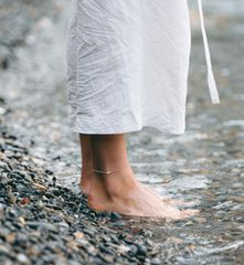 A woman in a white dress is standing barefoot in the water.
