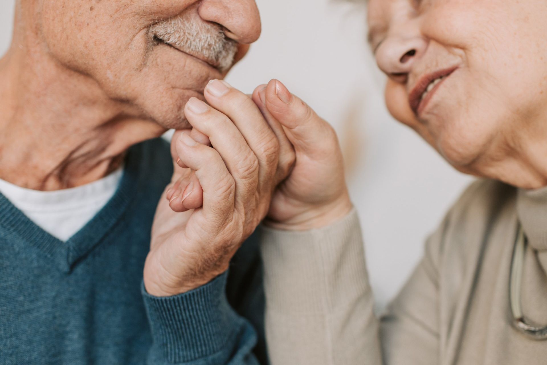 An elderly couple is holding hands and looking at each other.