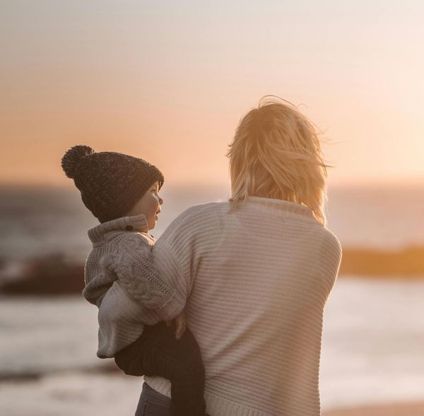 A woman and a child are holding hands while walking on the beach.