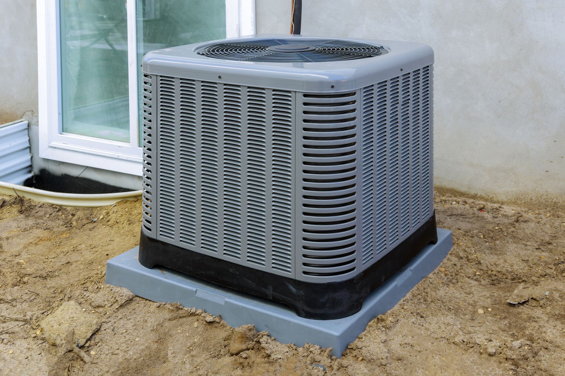 Outdoor air conditioner unit on a concrete pad beside a house wall