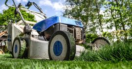 A blue and white lawn mower is sitting on top of a lush green lawn.