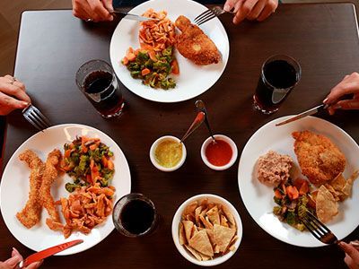 La gente está sentada en una mesa con platos de comida y bebidas.