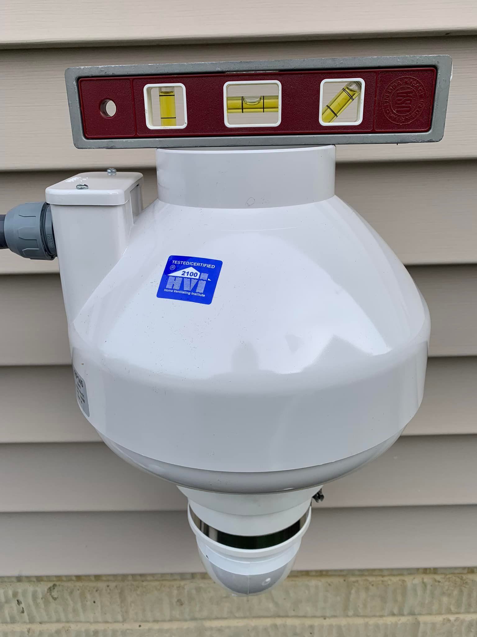 A white exhaust fan is mounted to the side of a house with a level.