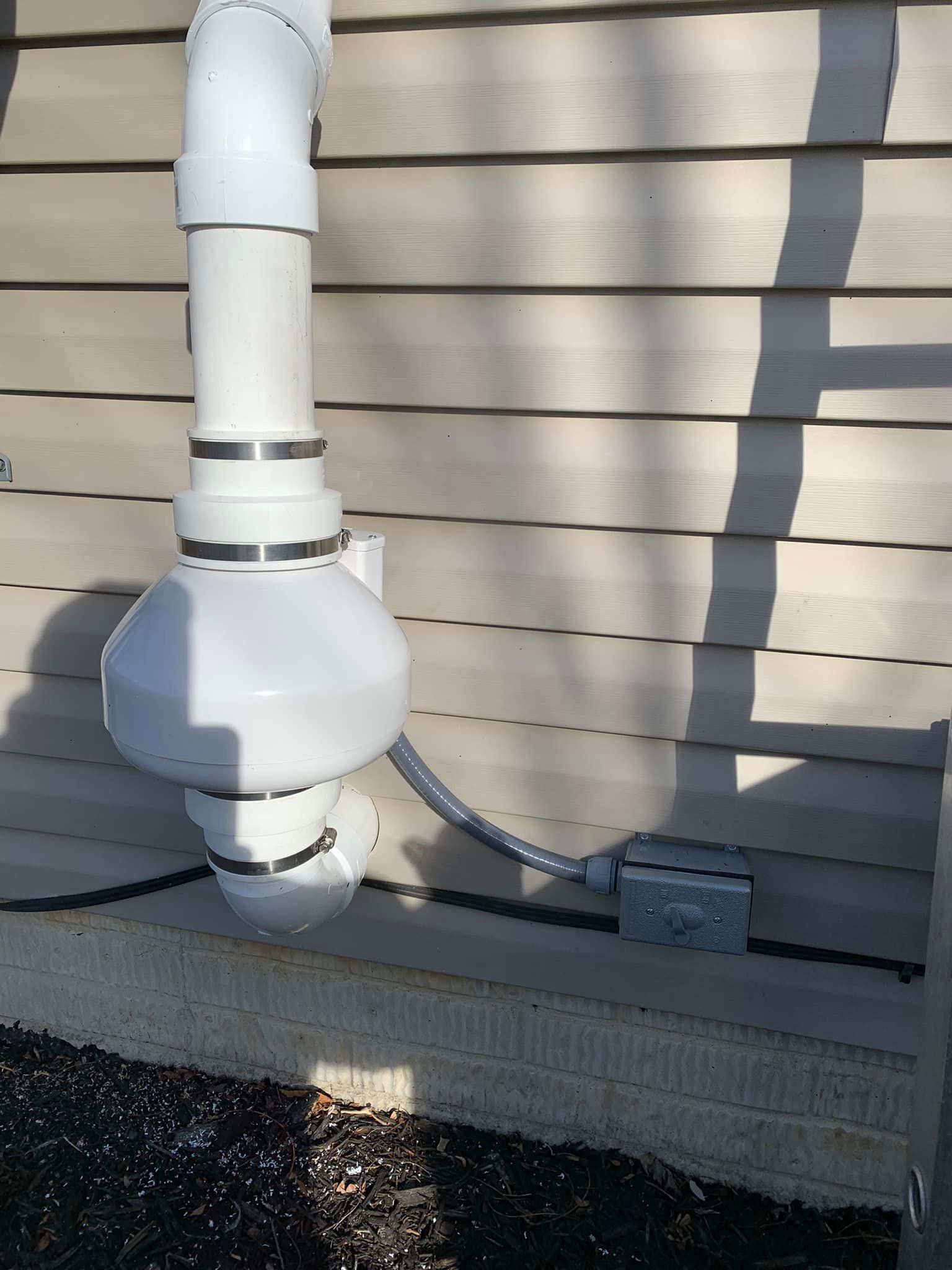 A white pipe is attached to the side of a house.