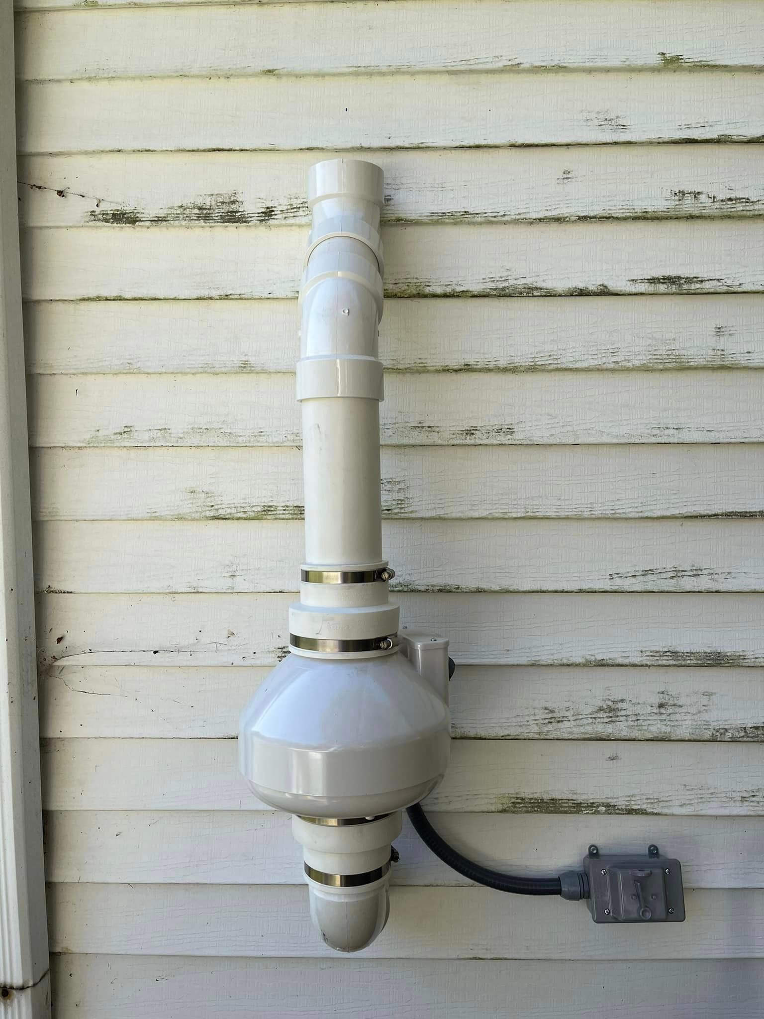 A white pipe is attached to the side of a house.