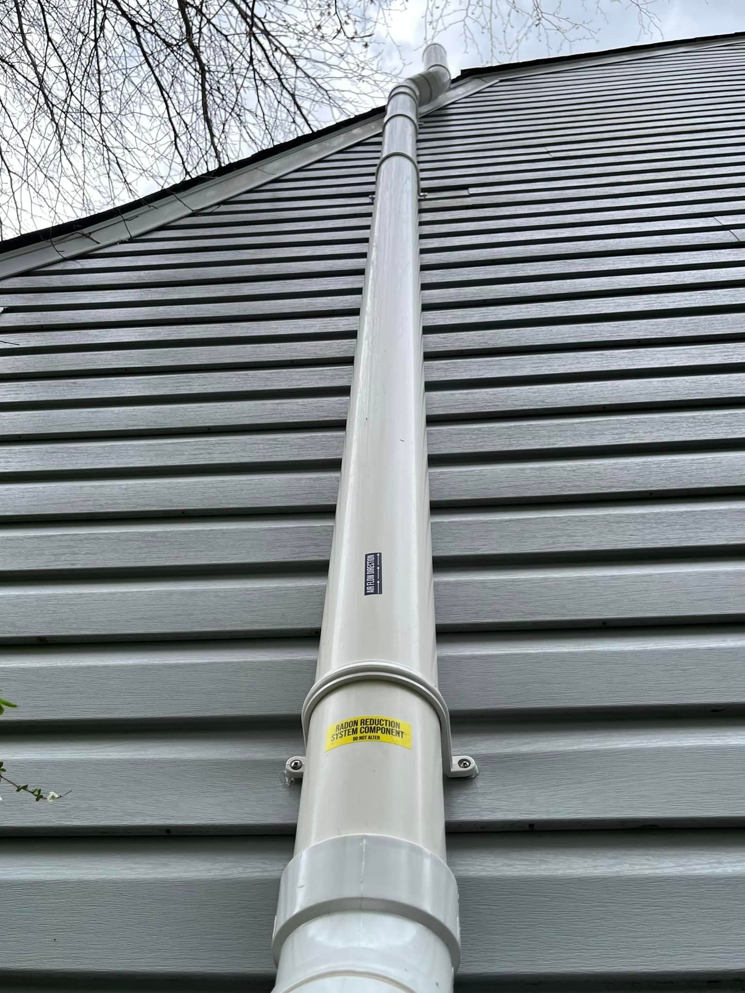 A white pipe is attached to the side of a house.
