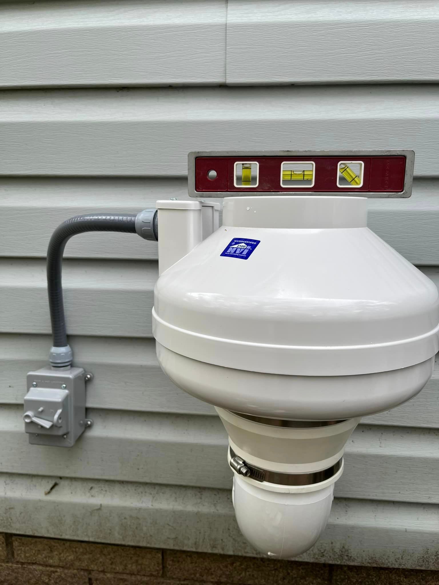A white toilet with a level attached to it is on the side of a house.