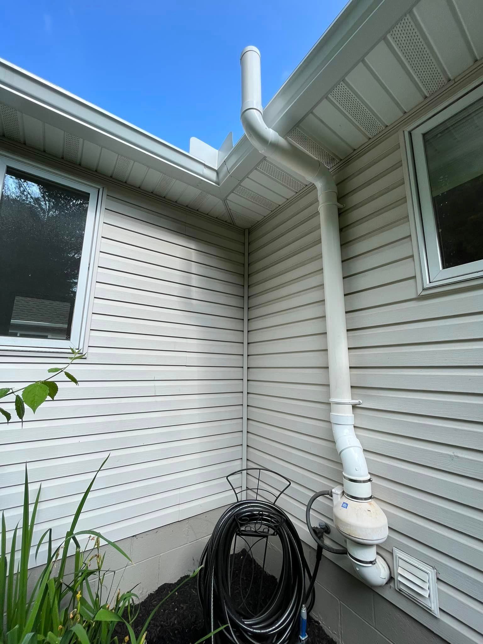 A hose is sitting on the side of a house next to a drain pipe.