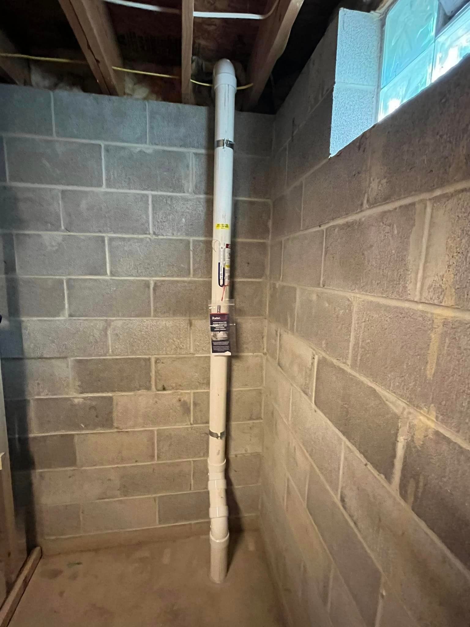 A white pipe is hanging from the ceiling in a basement next to a brick wall.