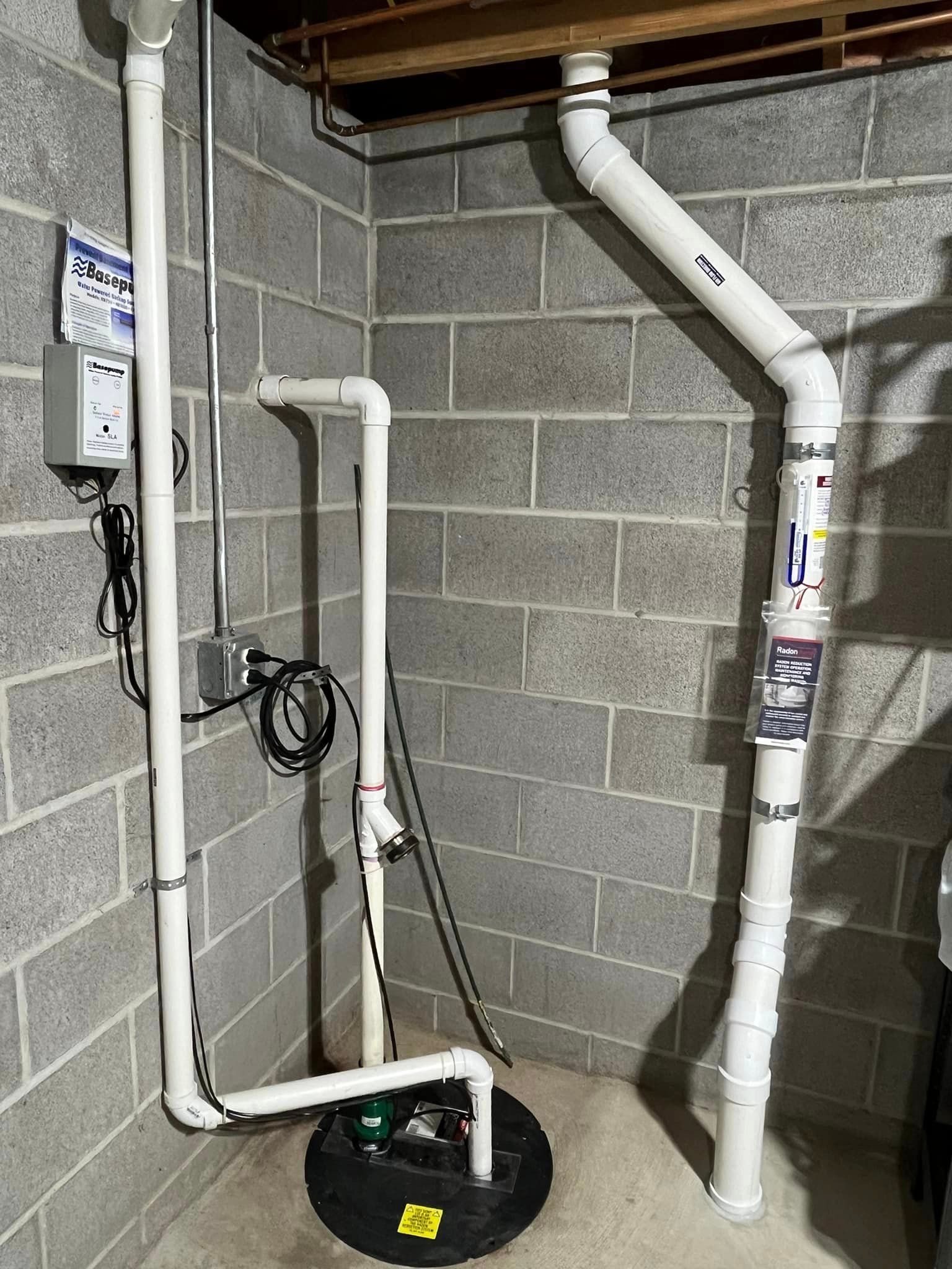 A basement with a sump pump and pipes.