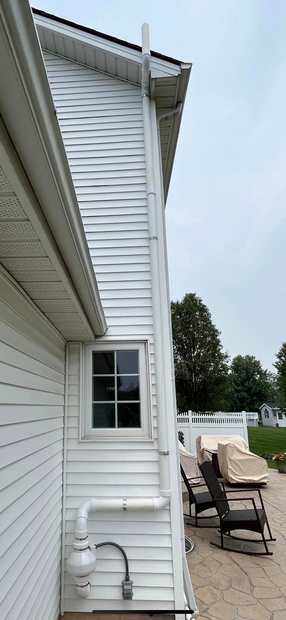 A white house with a drain pipe on the side of it.