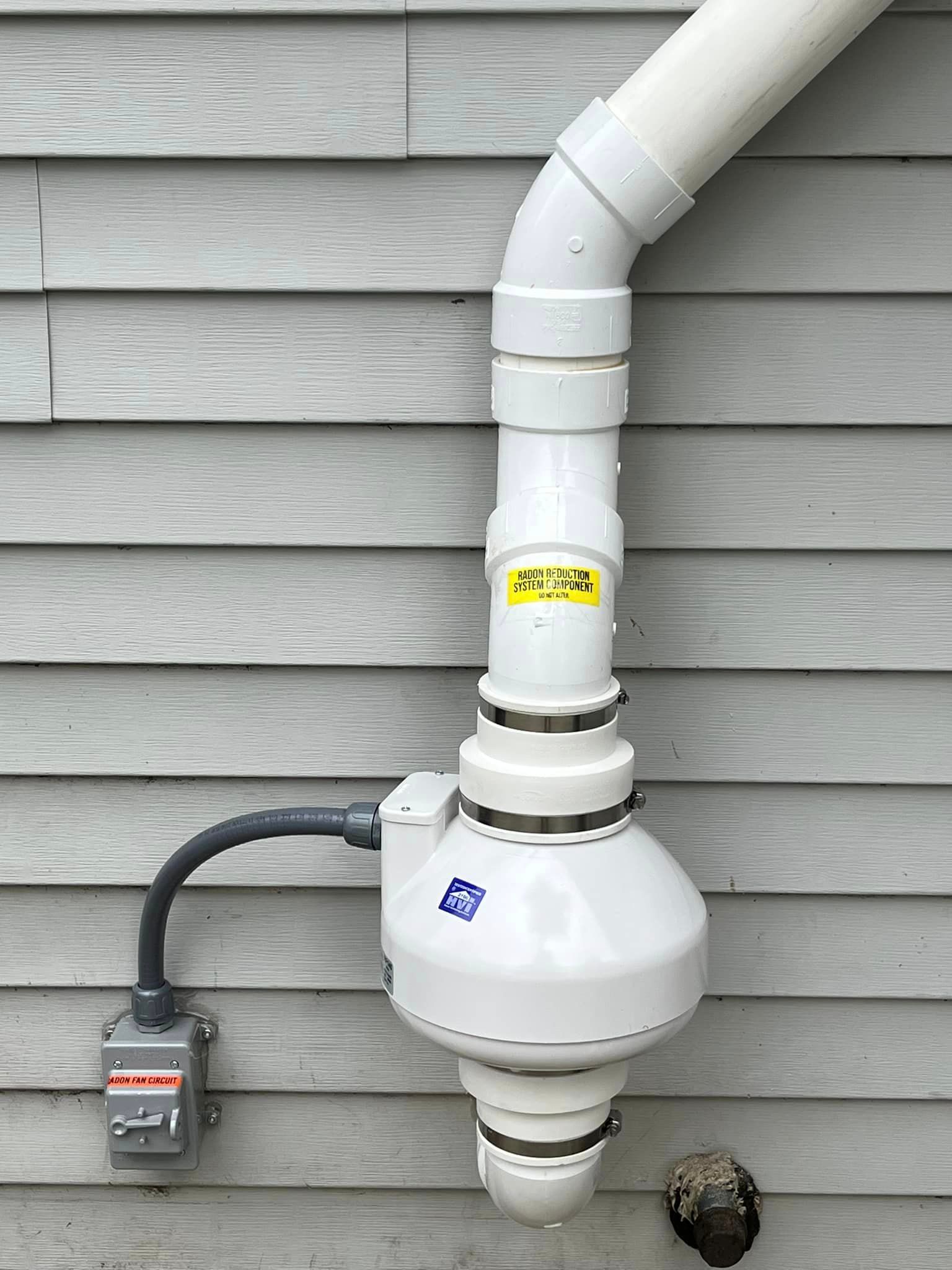 A white pipe is attached to the side of a house.